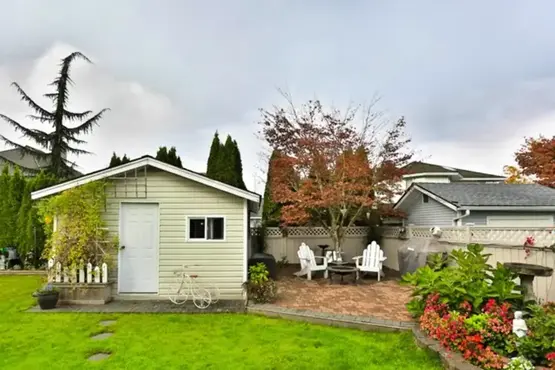 Beautiful custom backyard featuring a fire pit area shaded by trees, red paver patio, and surrounding flower landscaping.