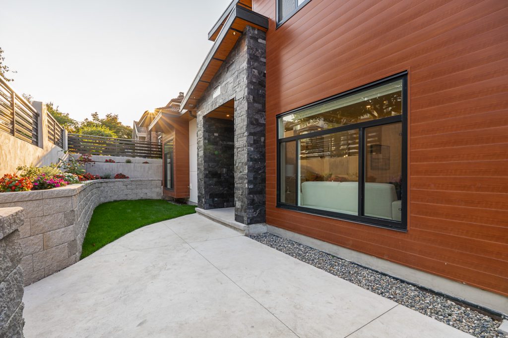 Sloped lot landscaping in Burnaby, British Columbia featuring custom curved concrete walking paths and beautifully designed curved Allan block planter retaining walls with integrated planting beds.