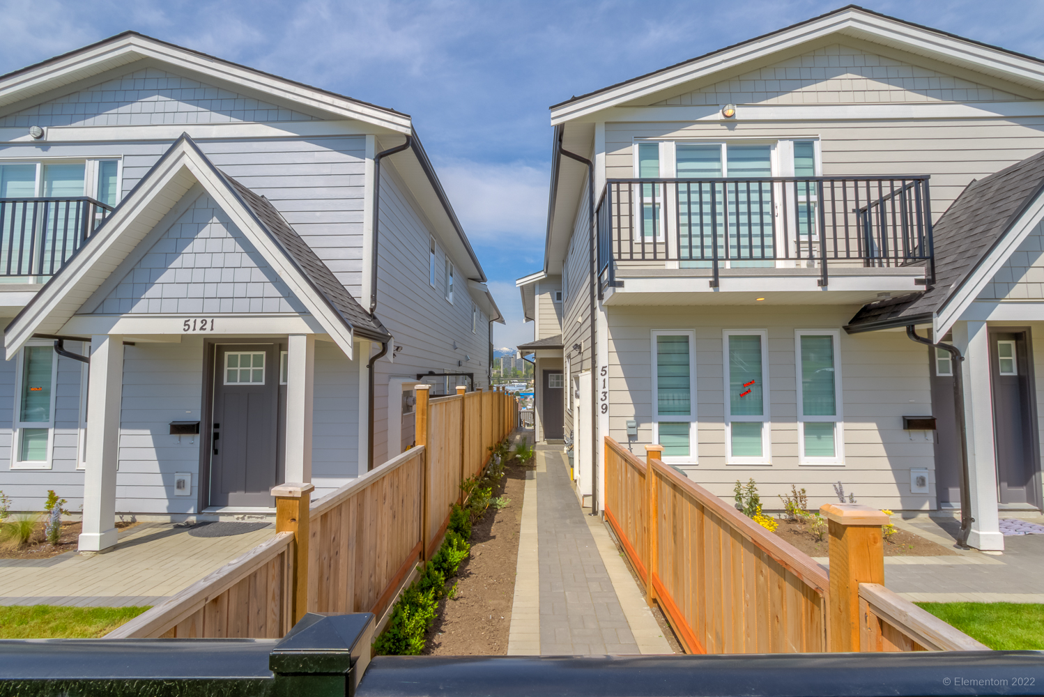 Custom cedar fencing on both sides of a walkway leading to the backyard, finished with grey pavers.