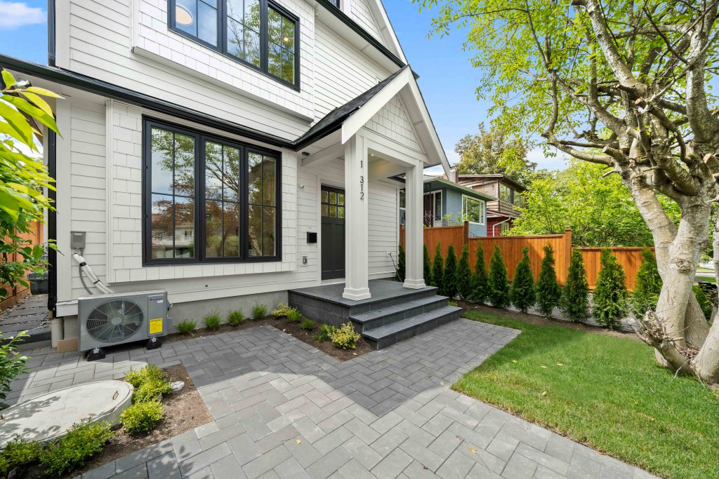 Farmhouse front yard with custom steps leading to the house, jet grey pavers with clean edges, and grass accents throughout the landscape.