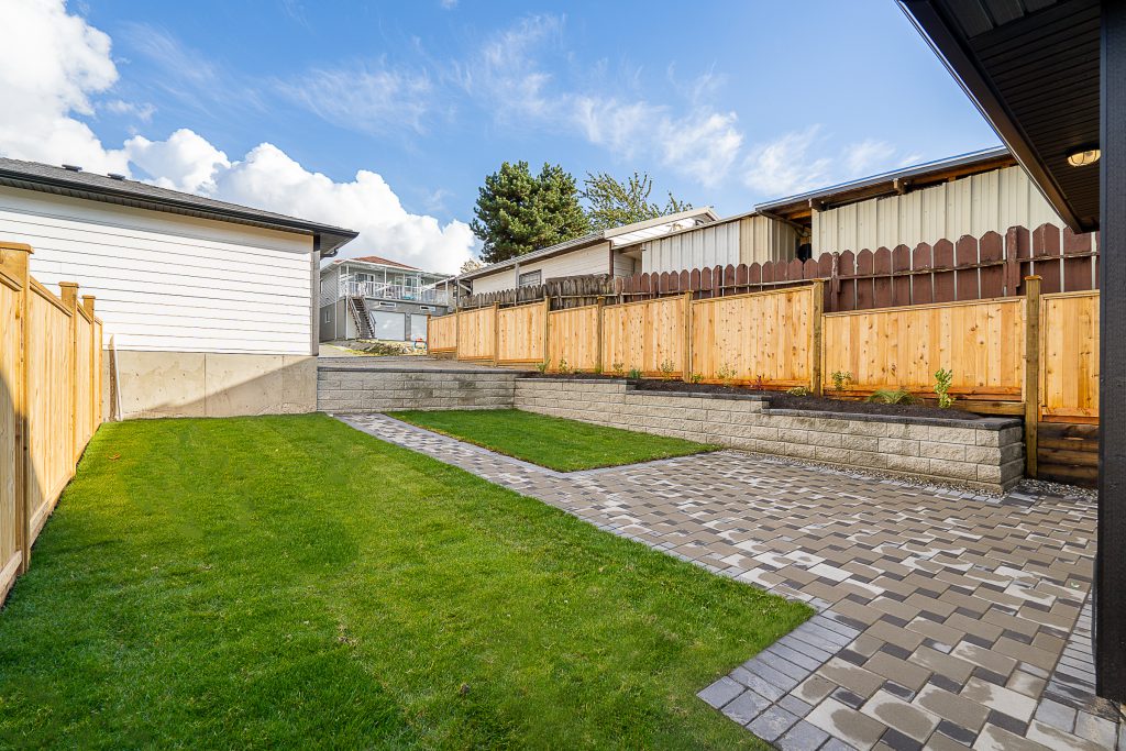 Backyard walkway in Richmond featuring an Allan block retaining wall, cedar fence, and lush green grass landscaping.