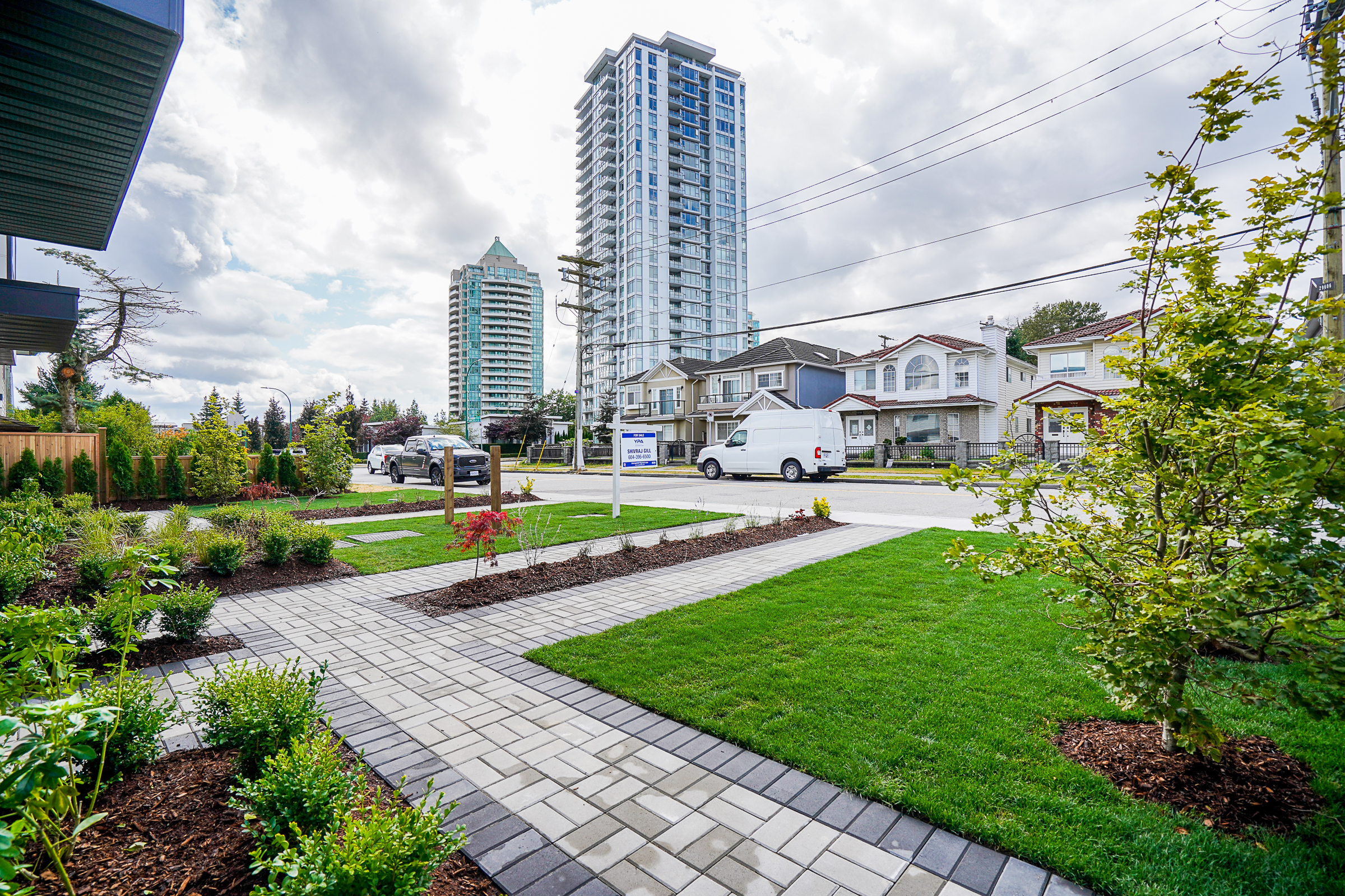 Paver walkway in Burnaby, British Columbia featuring beautifully landscaped shrubs and planted areas in a multiplex development with views of the city skyline.