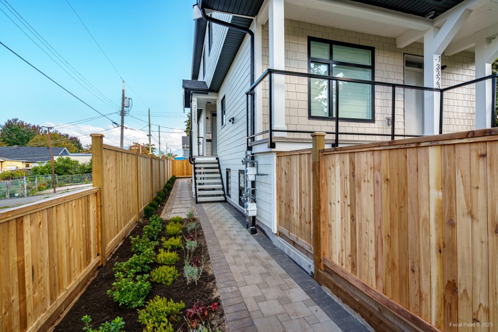 Coquitlam side walkway leading to house entrance with shrubs and custom tongue-and-groove cedar panels on both sides.