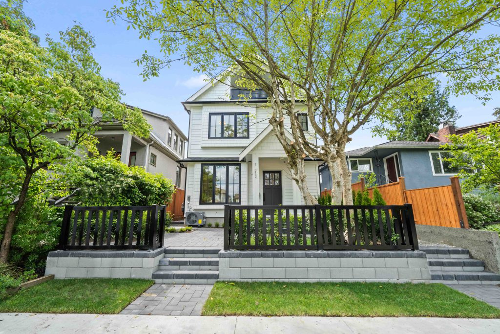 Vancouver farmhouse-style duplex with a smooth Allan Block retaining wall in the front yard, topped with a black aluminum fence, custom entry steps leading to the house, and a prominent decorative tree in the landscaping.